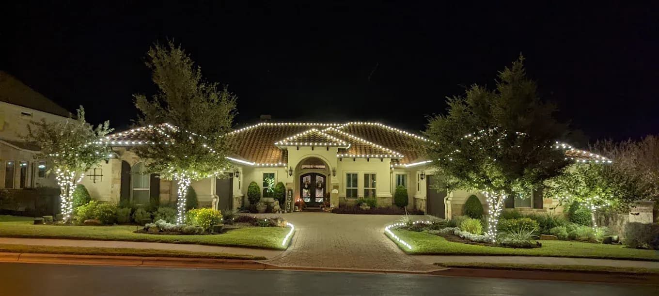 Vinings estate with continuous warm white lights along the roofline and matching wraps on front-yard trees